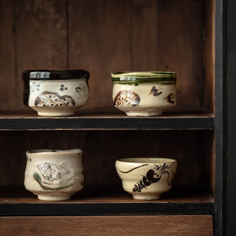 Handcrafted Japanese teacups with traditional patterns on a wooden shelf.