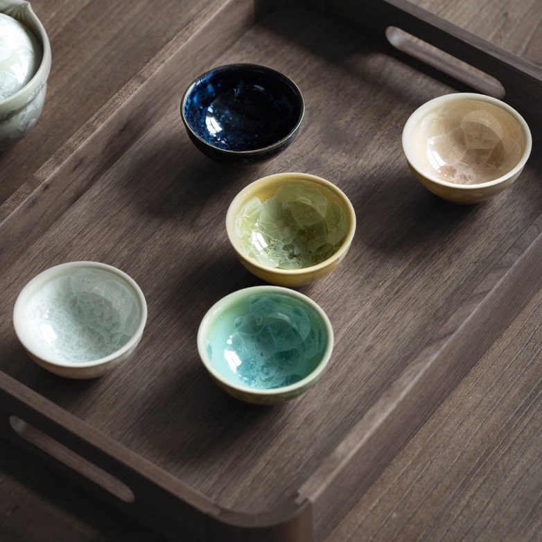 Vibrant tea cups in shades of blue, green, yellow, beige, and white with intricate crackle design.