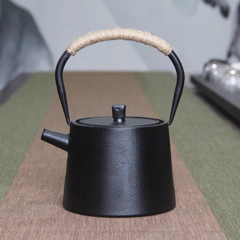 Close-up of the woven handle and sleek matte black finish on a cast iron tea pot.