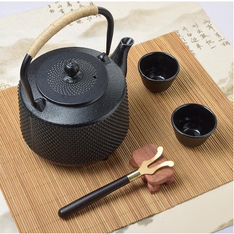 Black textured cast iron tea pot with matching cups on a bamboo mat.