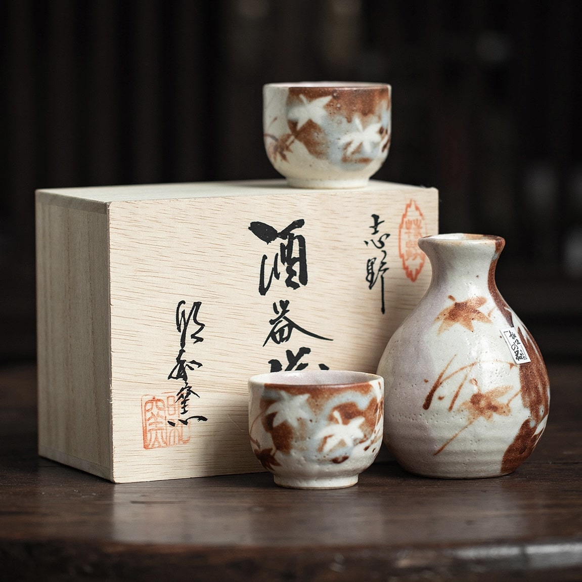 Ceramic sake set with hand-painted maple leaf designs on a wooden table