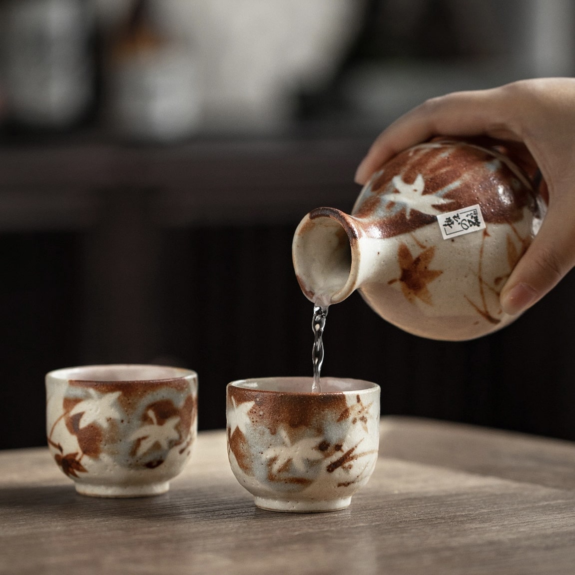 Ceramic sake set with hand-painted maple leaf designs on a wooden table