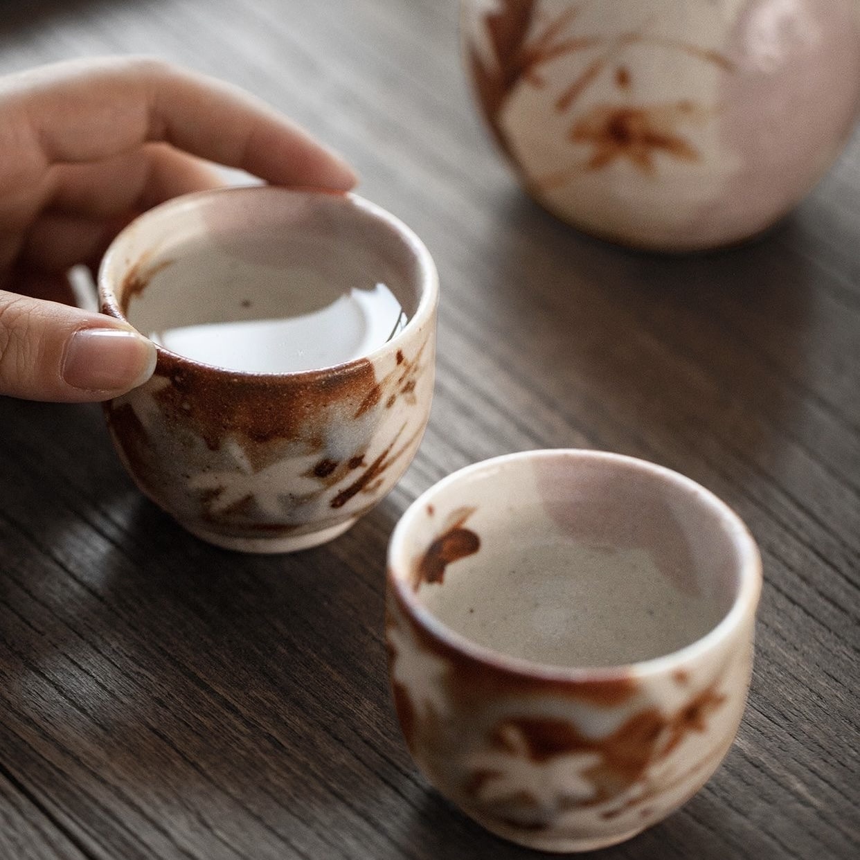 Hand holding a ceramic Ochoko cup filled with sake