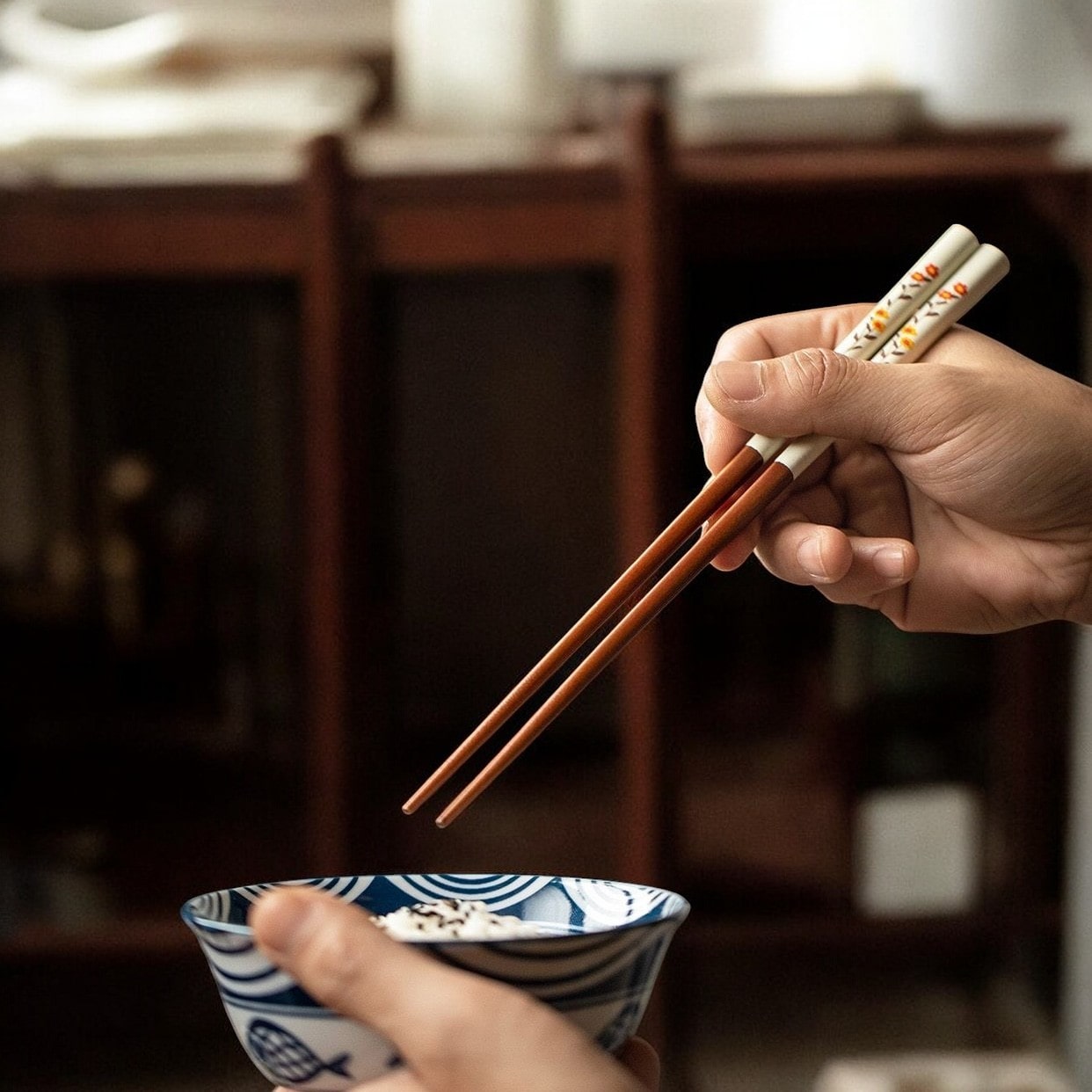 Hand holding a floral chopstick set above a rice bowl