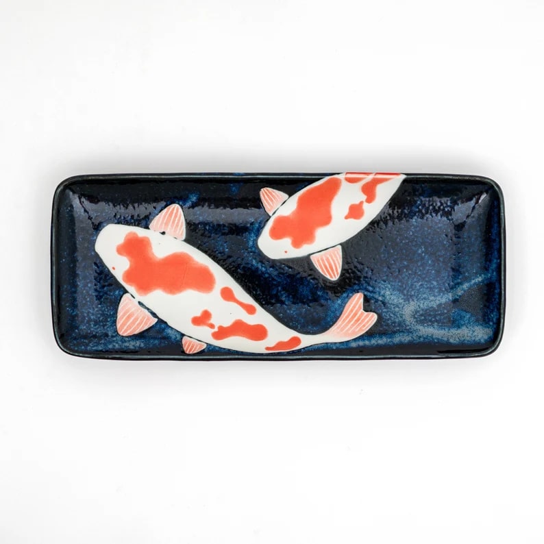 Close-up of hand-painted koi fish on a navy ceramic plate.
