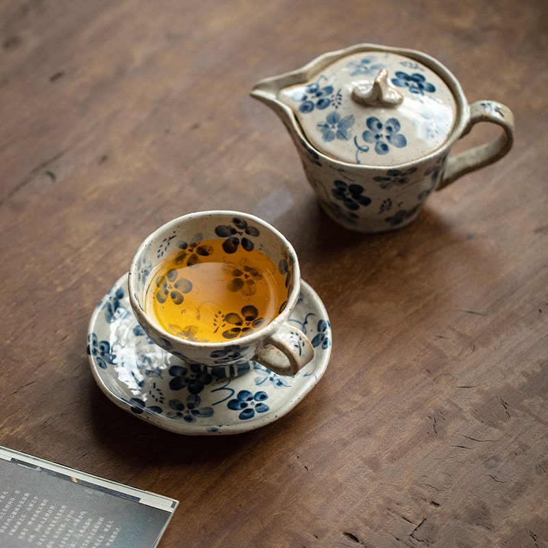 Tea being poured from a ceramic teapot into a matching floral teacup