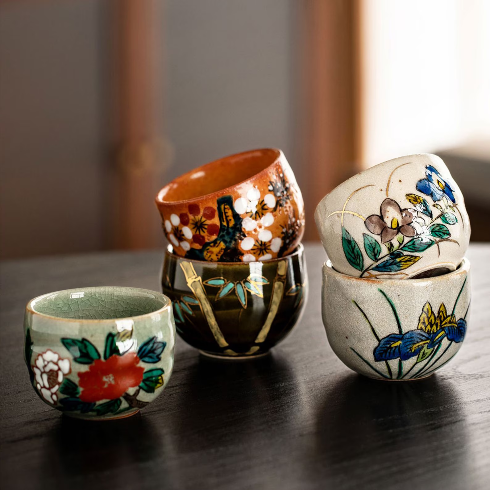 Stack of hand-painted Japanese tea cups with floral and nature motifs.
