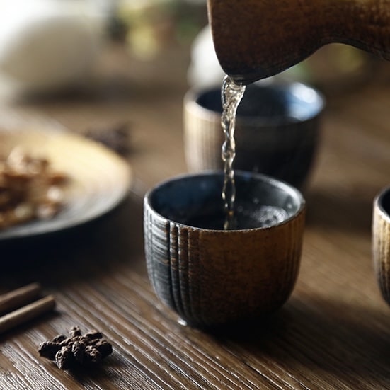 Rustic sake set with earthy and blue tones on a wooden table.
