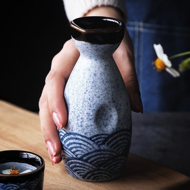 Speckled white sake bottle with matching cups featuring intricate designs.
