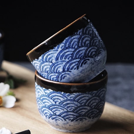 Speckled white sake bottle with matching cups featuring intricate designs.
