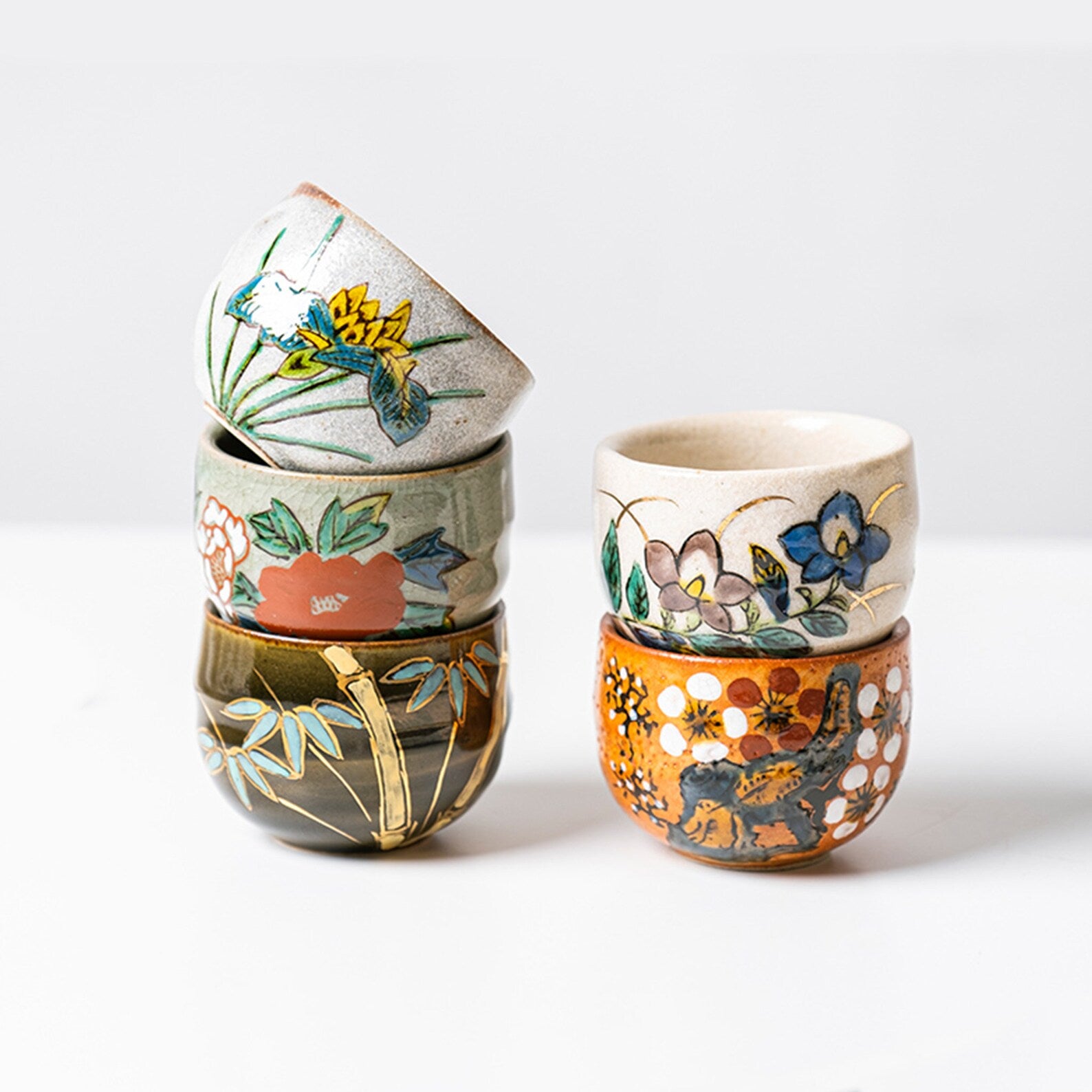 Stack of hand-painted Japanese tea cups with floral and nature motifs.
