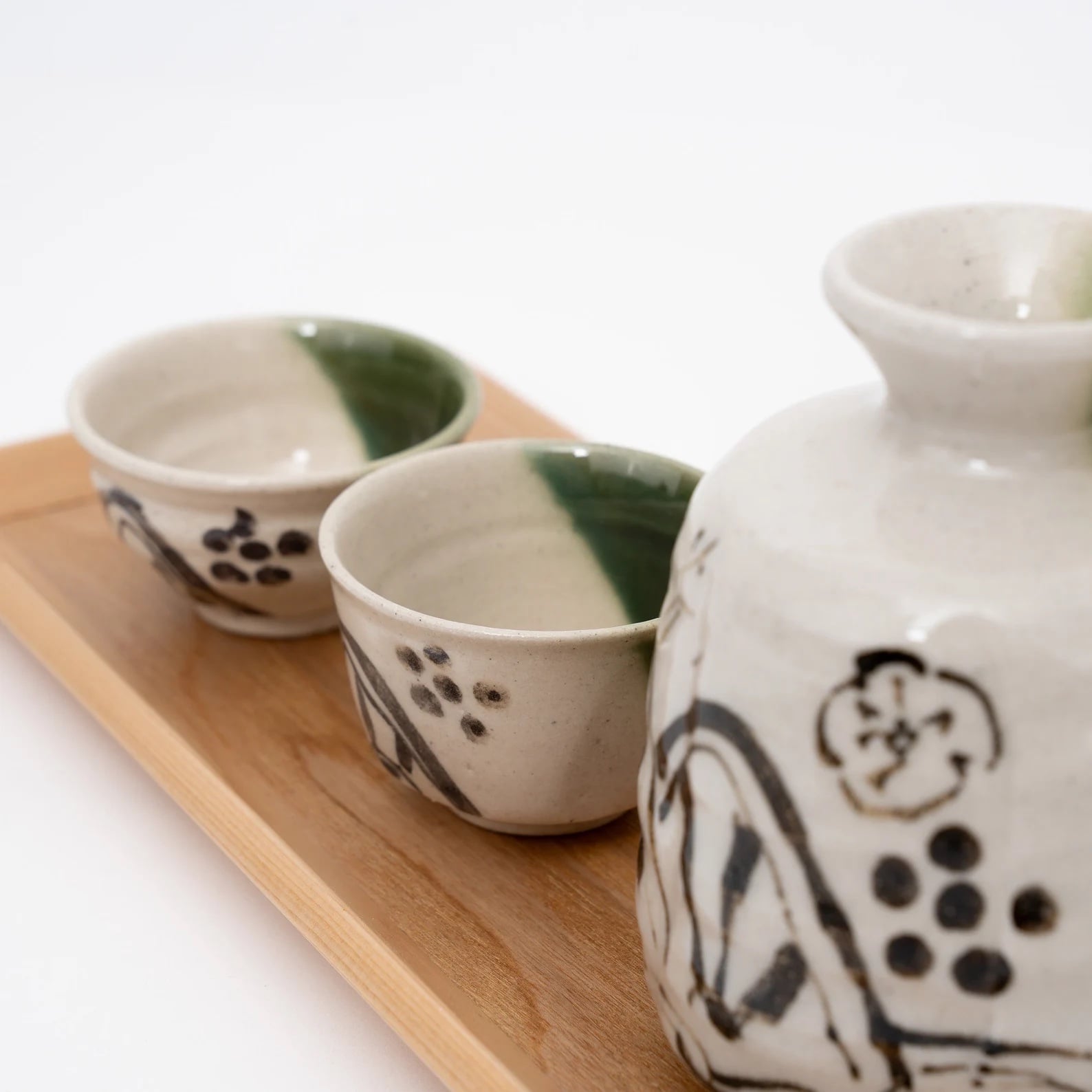 Two sake cups paired with a matching sake carafe on a wooden tray