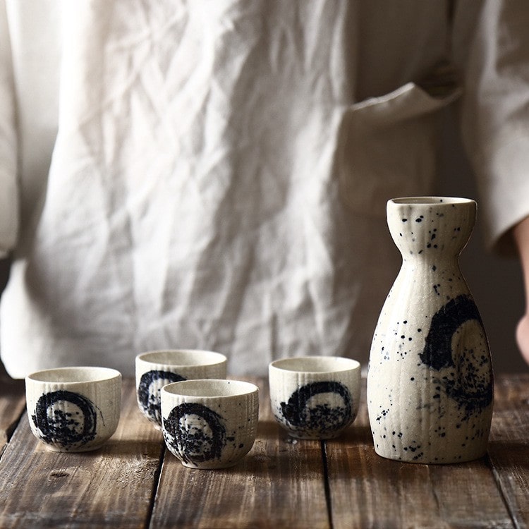 Artistic sake bottle and matching cups on a rustic wooden table.
