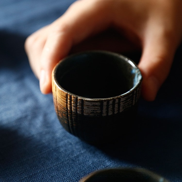 Full sake drinking set featuring a bottle and four cups on a navy cloth.
