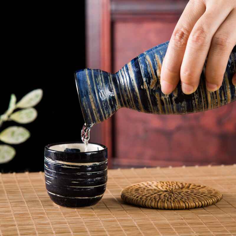 Handcrafted sake drinking set with a bottle and matching cups on a bamboo mat.
