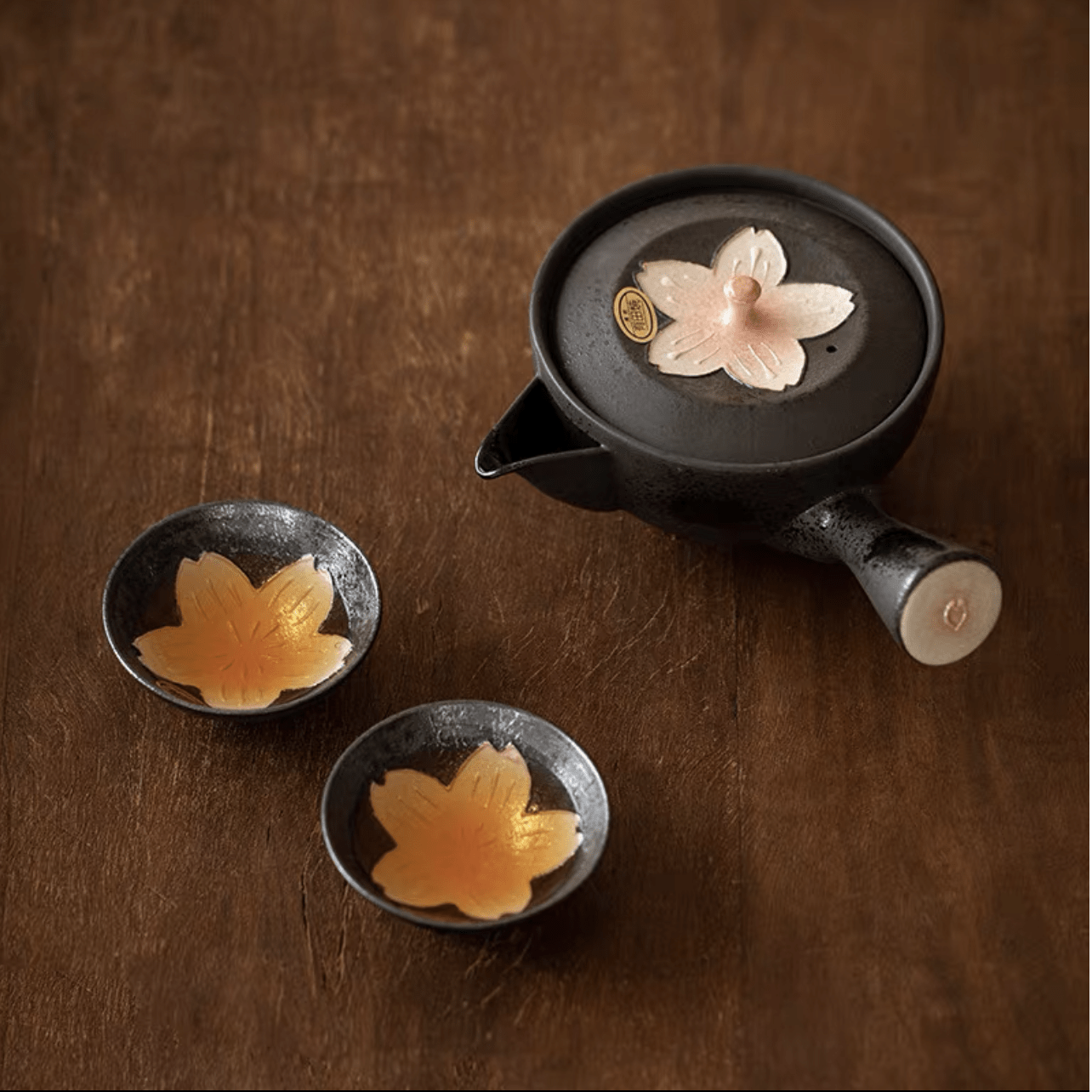 Black kyusu teapot with pink sakura blossom motif and matching teacups on a wooden surface.